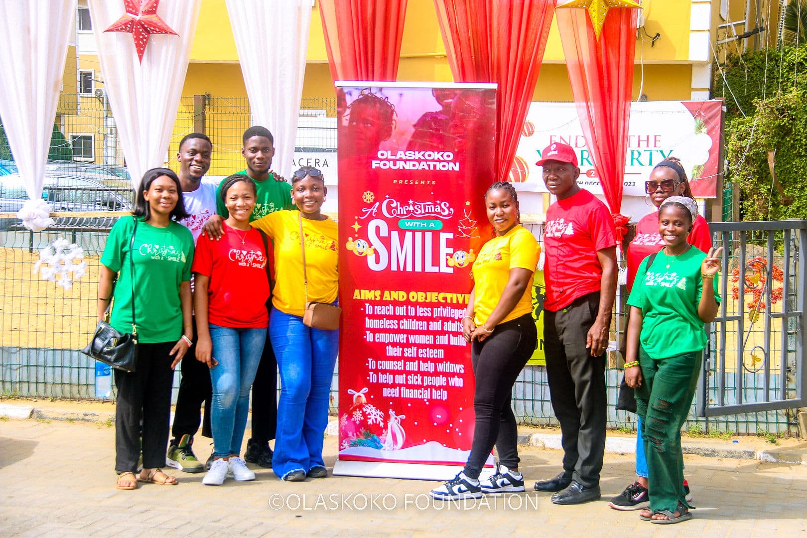 Volunteers in Olaskoko t-shirts beside the Christmas With A Smile banner